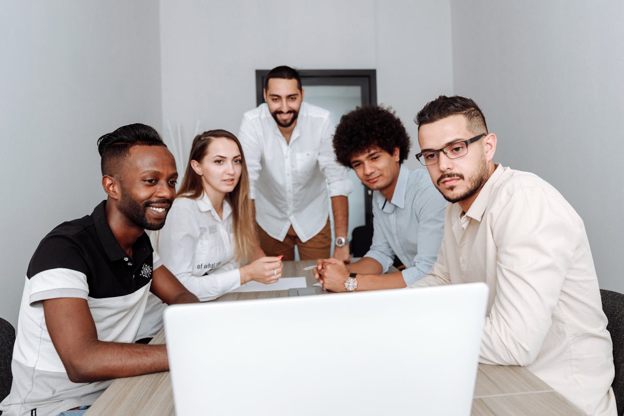 A diverse group of professionals engaging in a collaborative meeting around a laptop in an office.